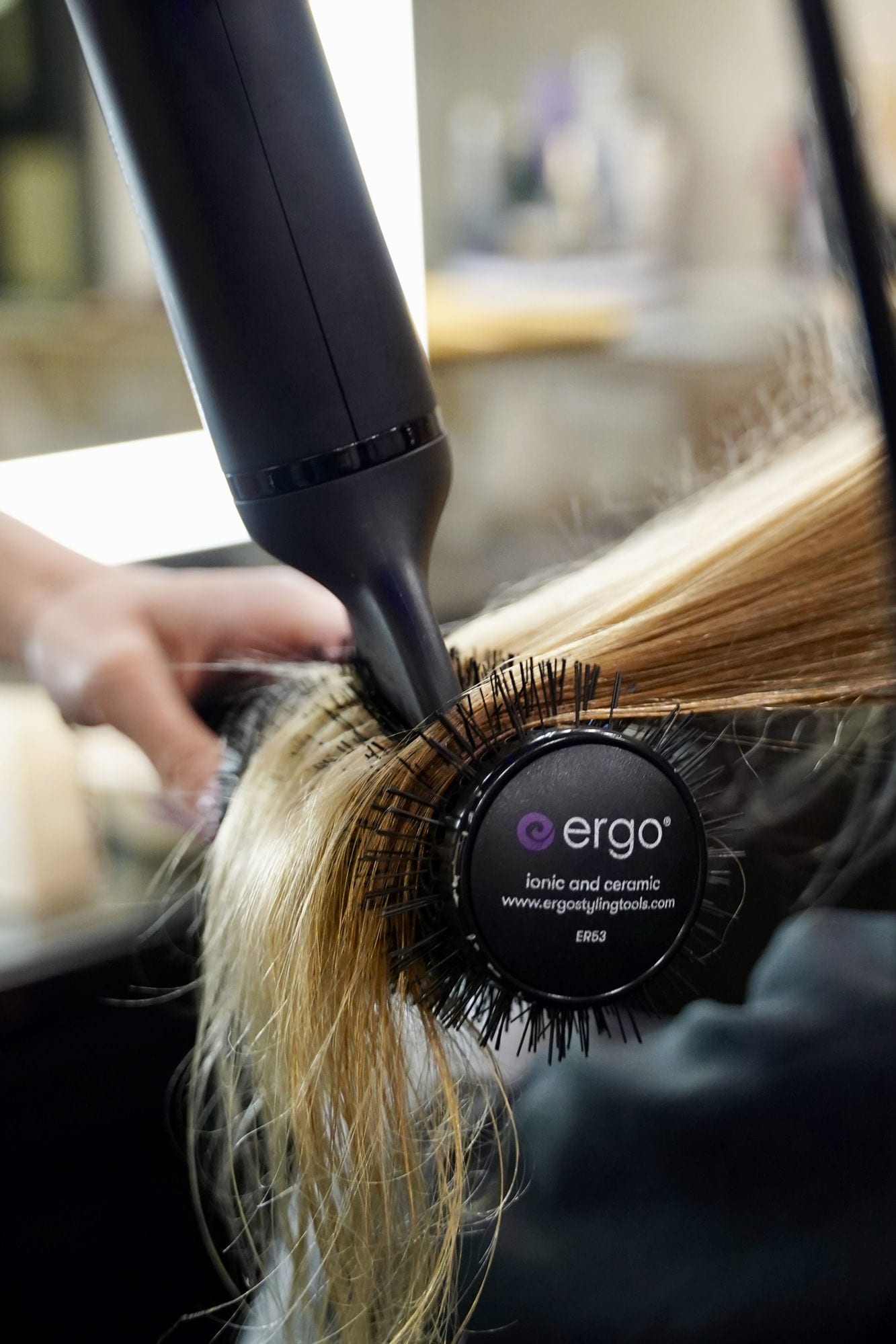 A stylist blowing out long blonde hair with a round brush at Salon on 3rd